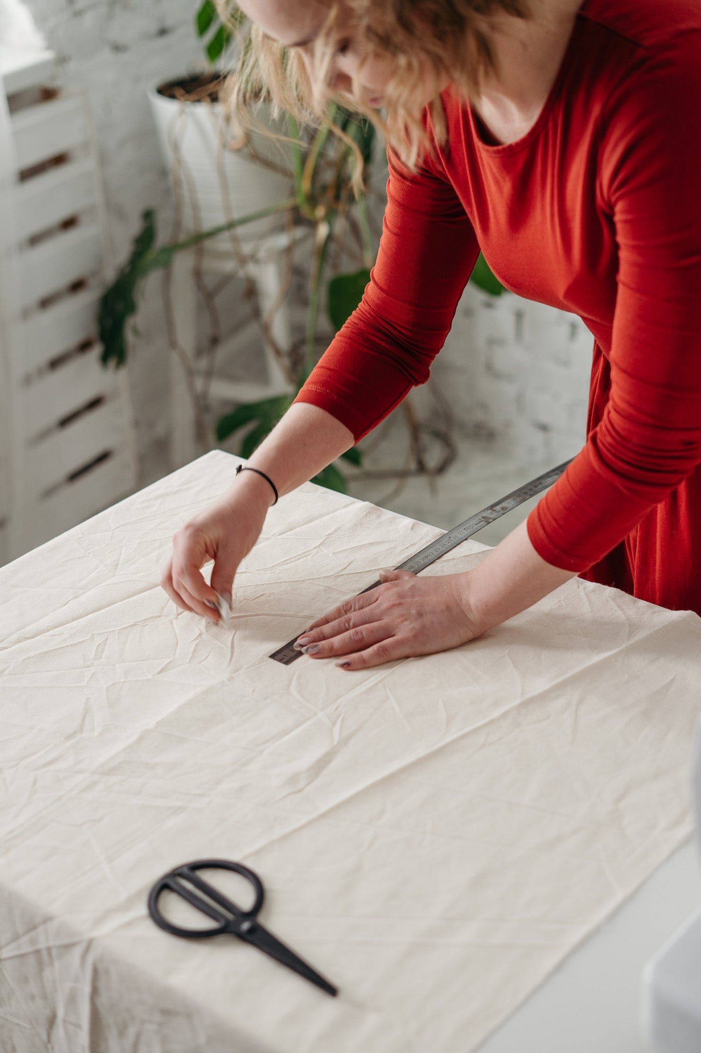 A woman in a red top is using tailors chalk to draw a pattern on canvas